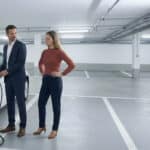 Mann in Anzug lädt ein E-Auto in einer Tiefgarage während eine Frau daneben wartet